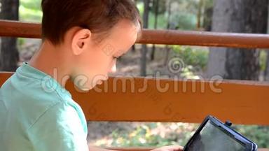 秋天公园里有平板电脑的青少年。 学龄前儿童，小学生在阳台上玩平板电脑，或者